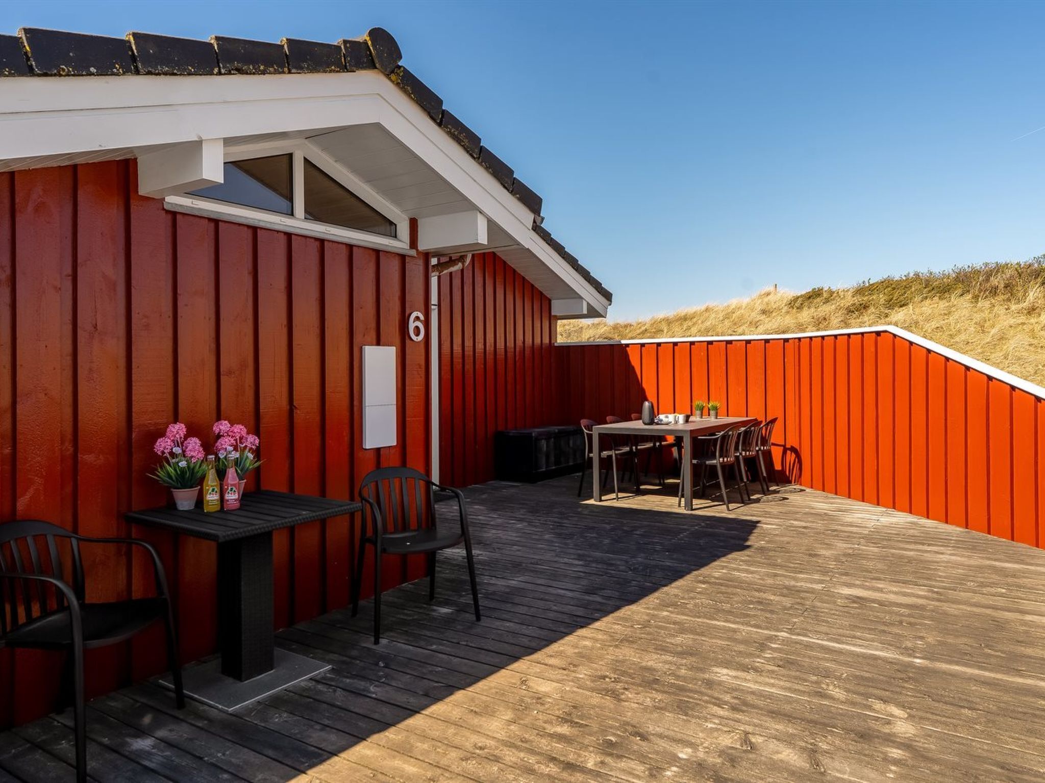 Un bâtiment rouge avec une terrasse en bois, une table entourée de chaises et des plantes en pot.