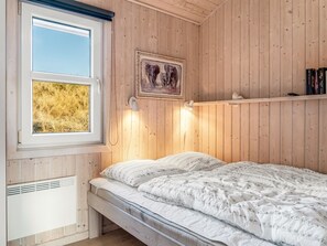 Un dormitorio con cama, ventana con vistas a un campo de heno, un cuadro enmarcado y una estantería con libros.