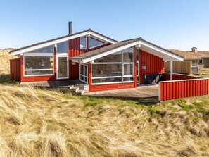 A modern house with large windows, a wooden deck, and a red exterior.