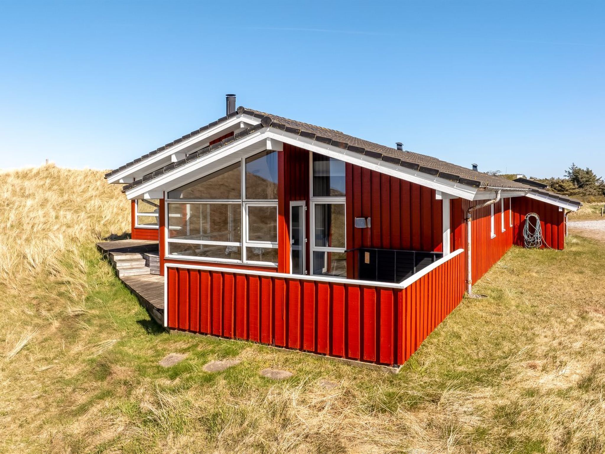 A red building with a large glass window, a white roof, and a wooden deck.
