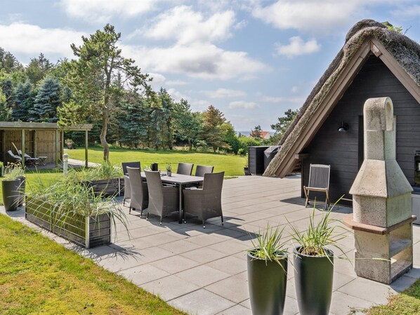 An outdoor patio with a table and chairs, a stone fireplace, and a thatched-roof structure.