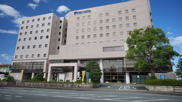 A modern hotel building with multiple floors, a prominent 'FLEX HOTEL' sign, and a well-maintained entrance area with greenery. - FREX HOTEL (Matsusaka)