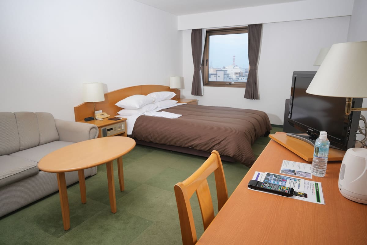 Une chambre d’hôtel équipée d’un lit, d’un canapé, d’une table, d’une télévision et d’une fenêtre donnant sur la ville.