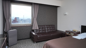 A hotel room with a large window, a leather sofa, a bed, a bedside table with a lamp, and a small desk with a computer. - FREX HOTEL (Matsusaka)