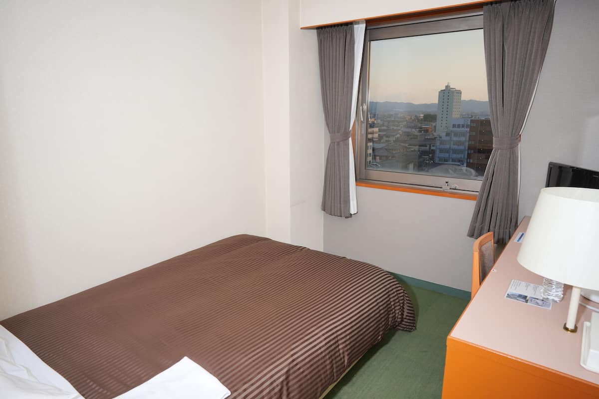 Une chambre d’hôtel avec un lit, un bureau doté d’une lampe et une fenêtre avec des rideaux.