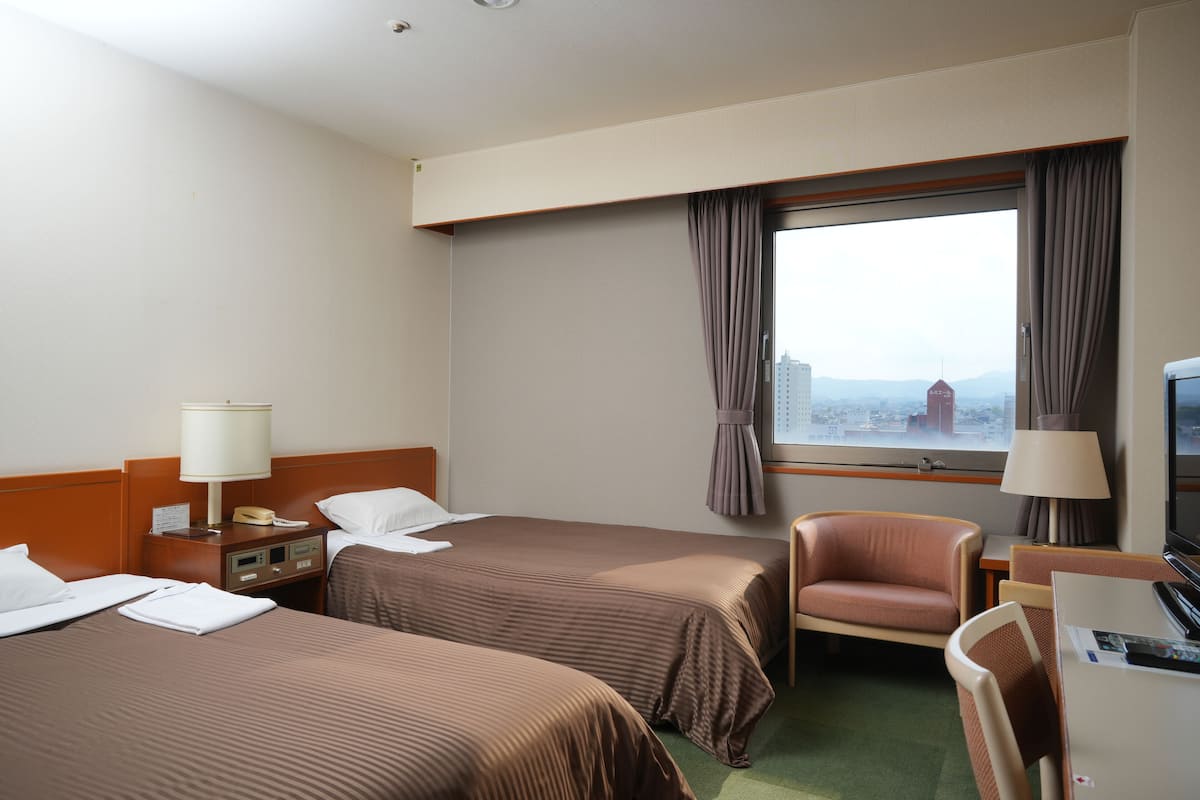 Une chambre d’hôtel avec deux lits, un bureau avec une chaise, une télévision et une fenêtre avec des rideaux.
