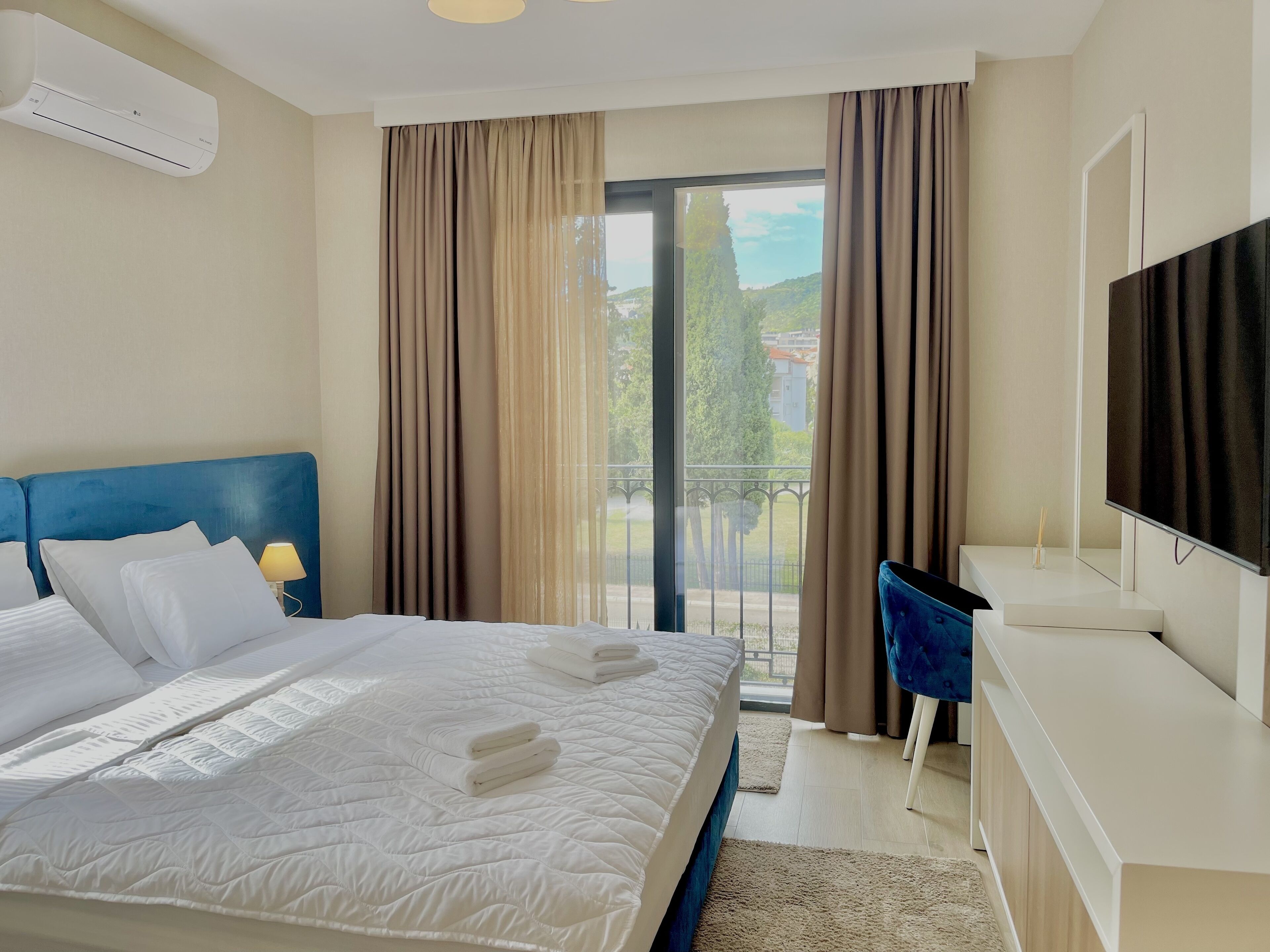 A hotel room with a bed, a desk, a TV, and a balcony with curtains.