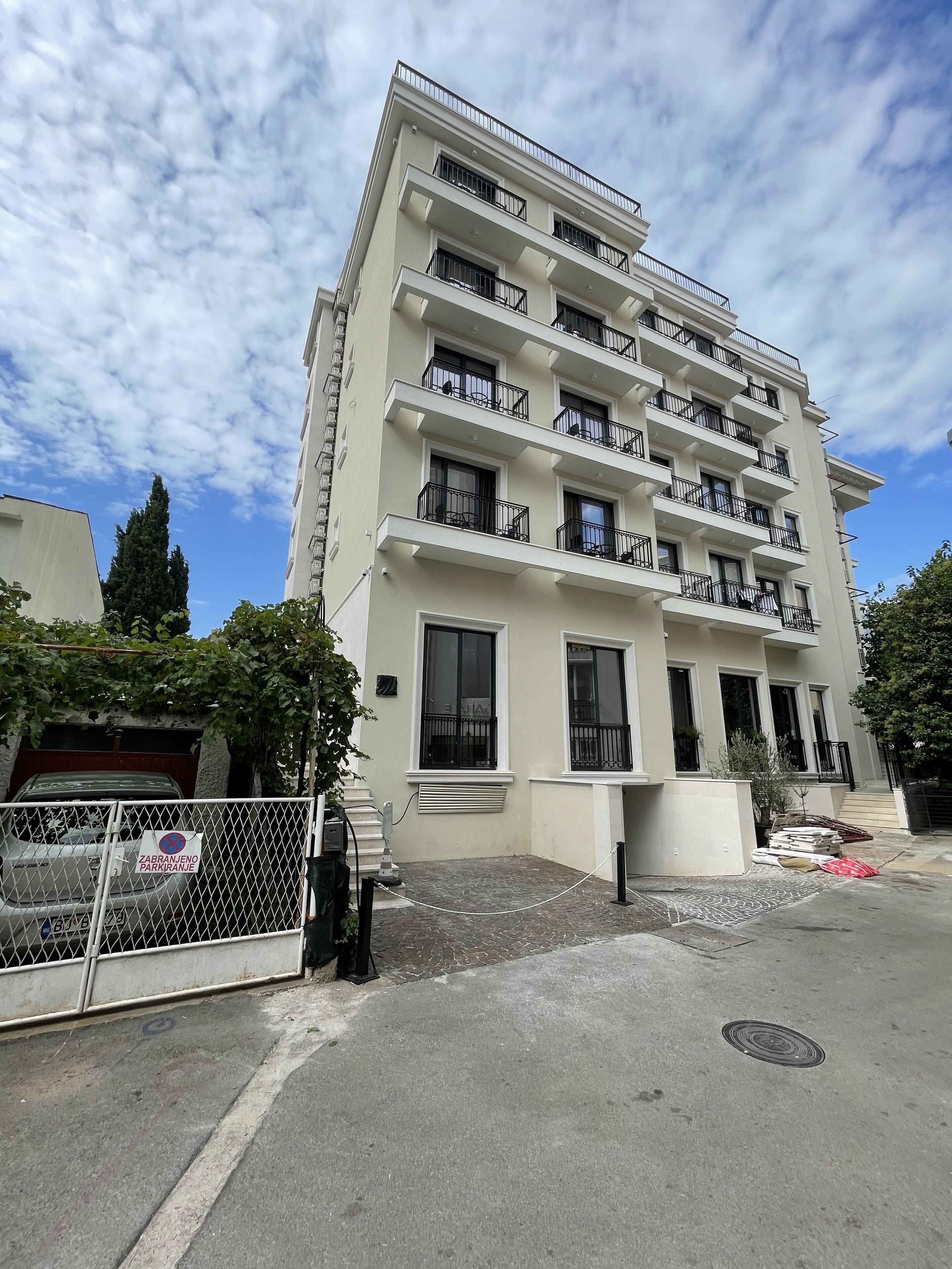 A multi-story residential building with balconies, a gated parking area, and a clear sky.