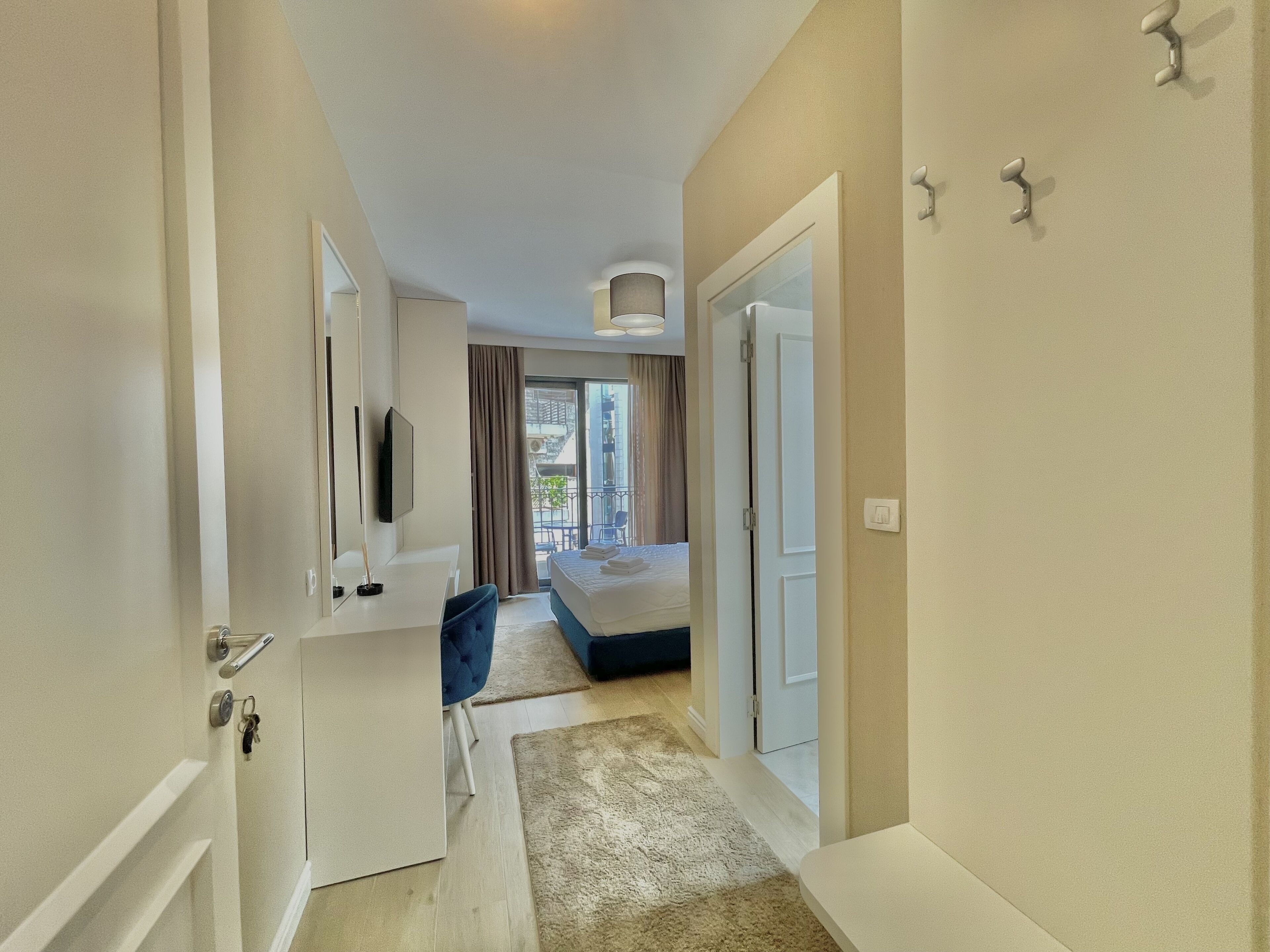 A modern hotel room with a bed, a desk, a chair, a TV, and a bathroom.