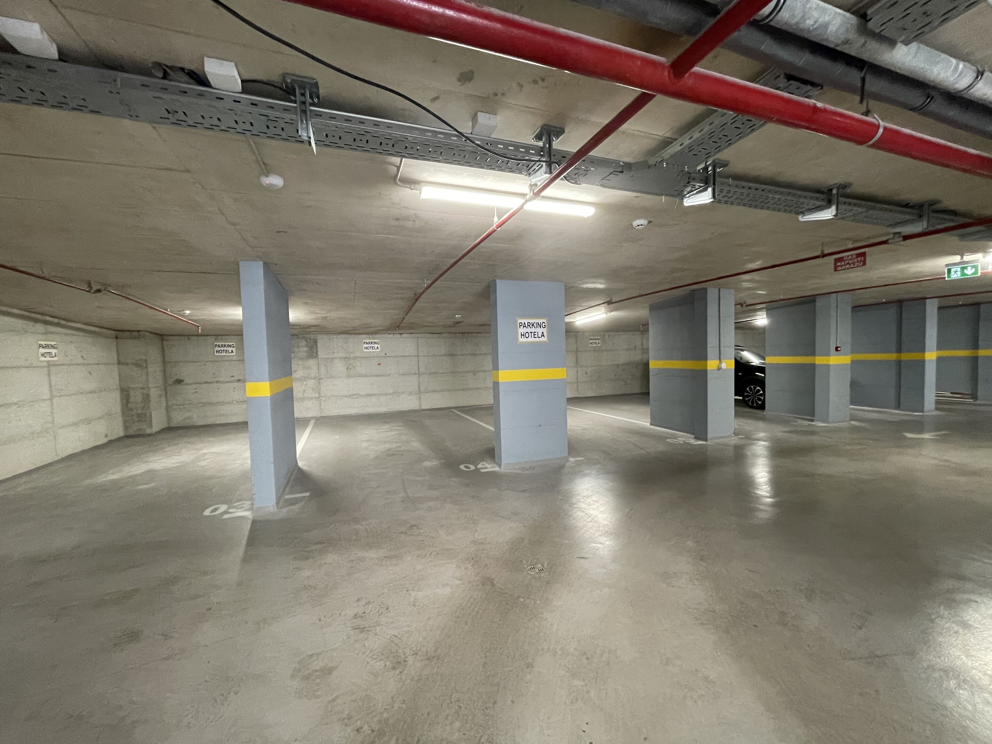 A parking garage with concrete pillars, yellow lines, and signs indicating parking for hotel guests.