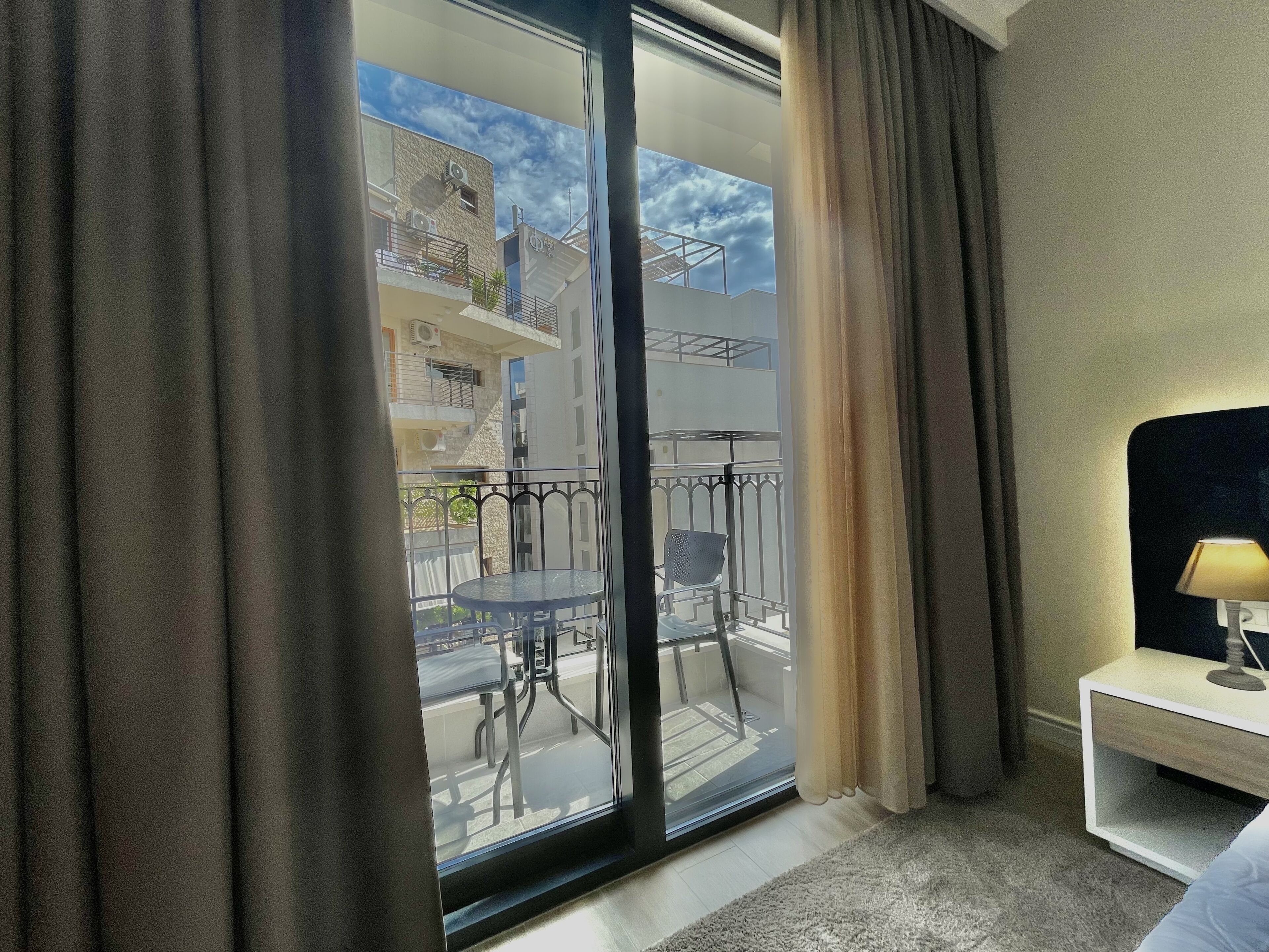 Habitación de hotel con un amplio ventanal corredizo que da a un balcón con mesa y sillas.