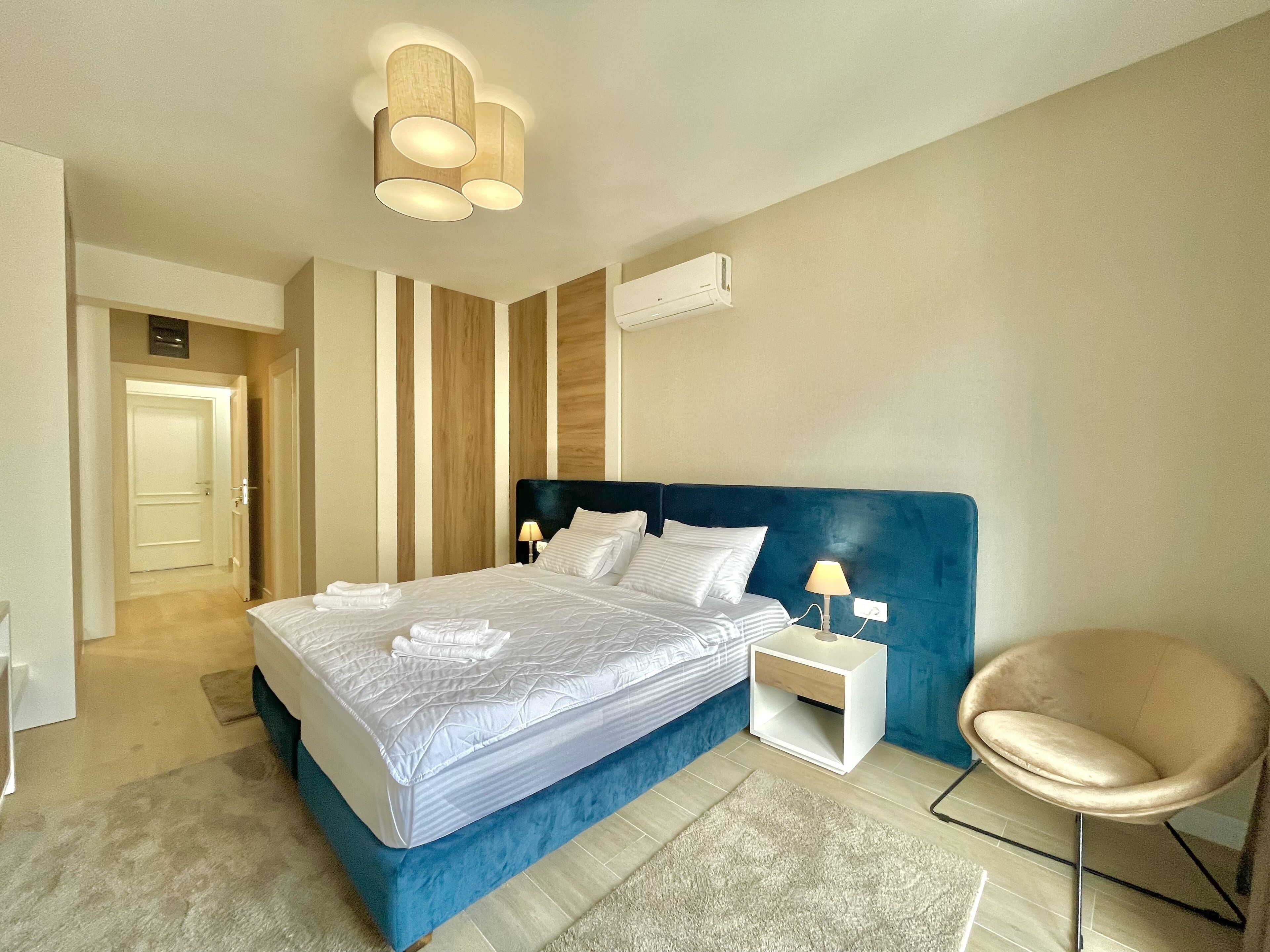 Ein modernes Schlafzimmer mit einem großen Bett, einem Nachttisch mit Lampe, einem Sessel und einer Klimaanlage an der Wand.