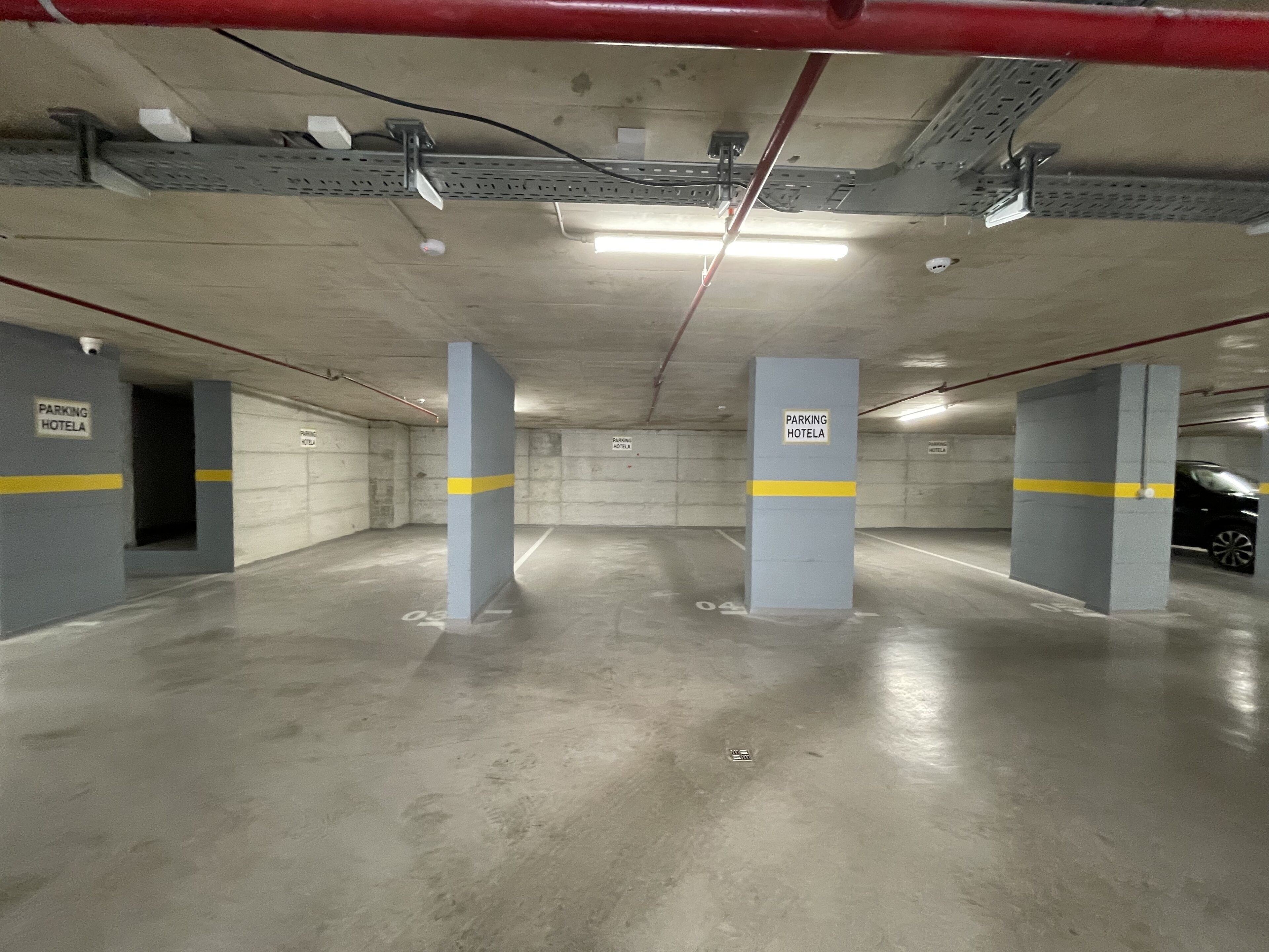 A parking garage with concrete pillars, fluorescent lighting, and signs indicating a parking area for a hotel.