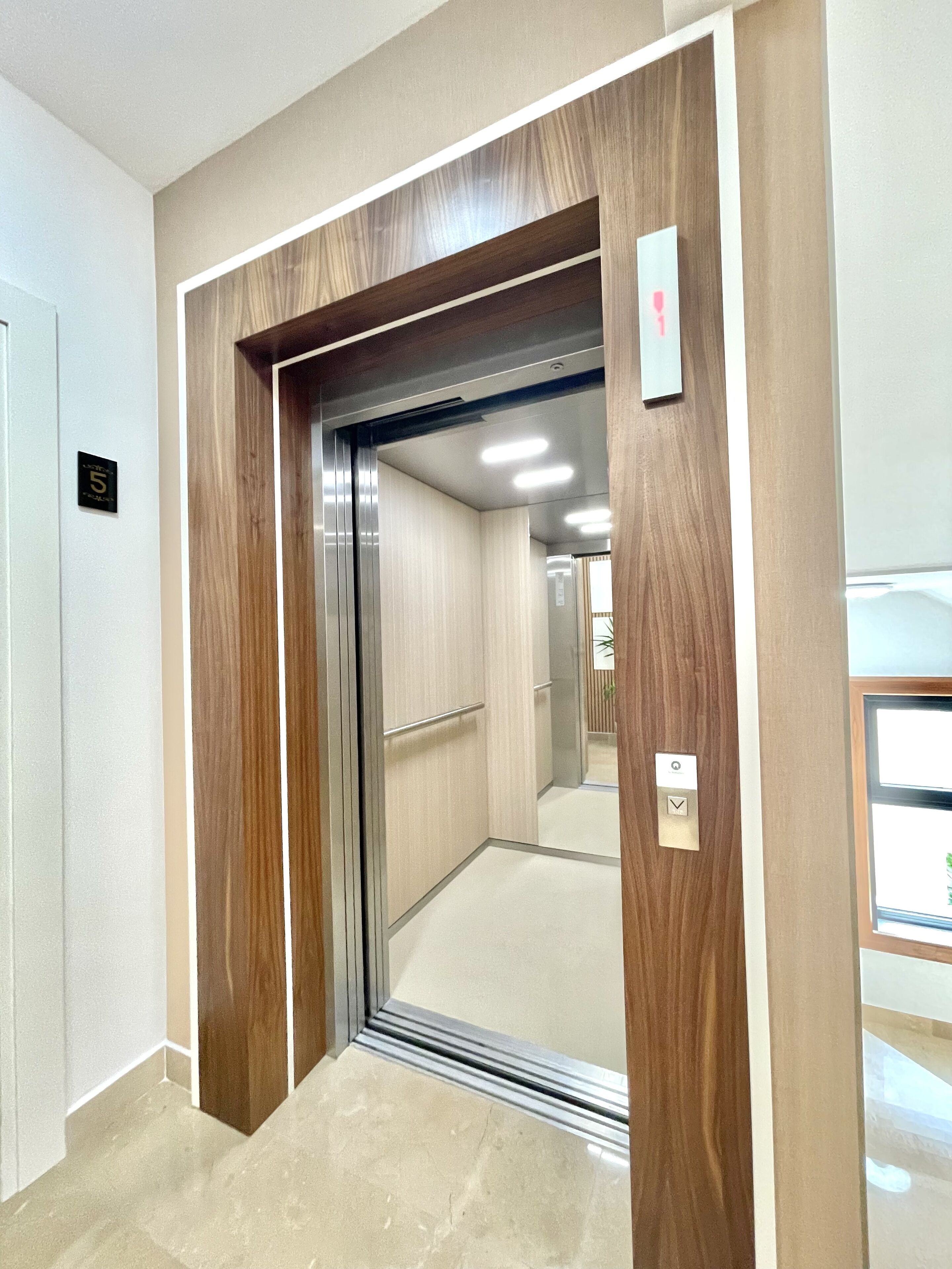 An elevator with a wooden frame and a metallic door, a light switch, and a floor number sign.