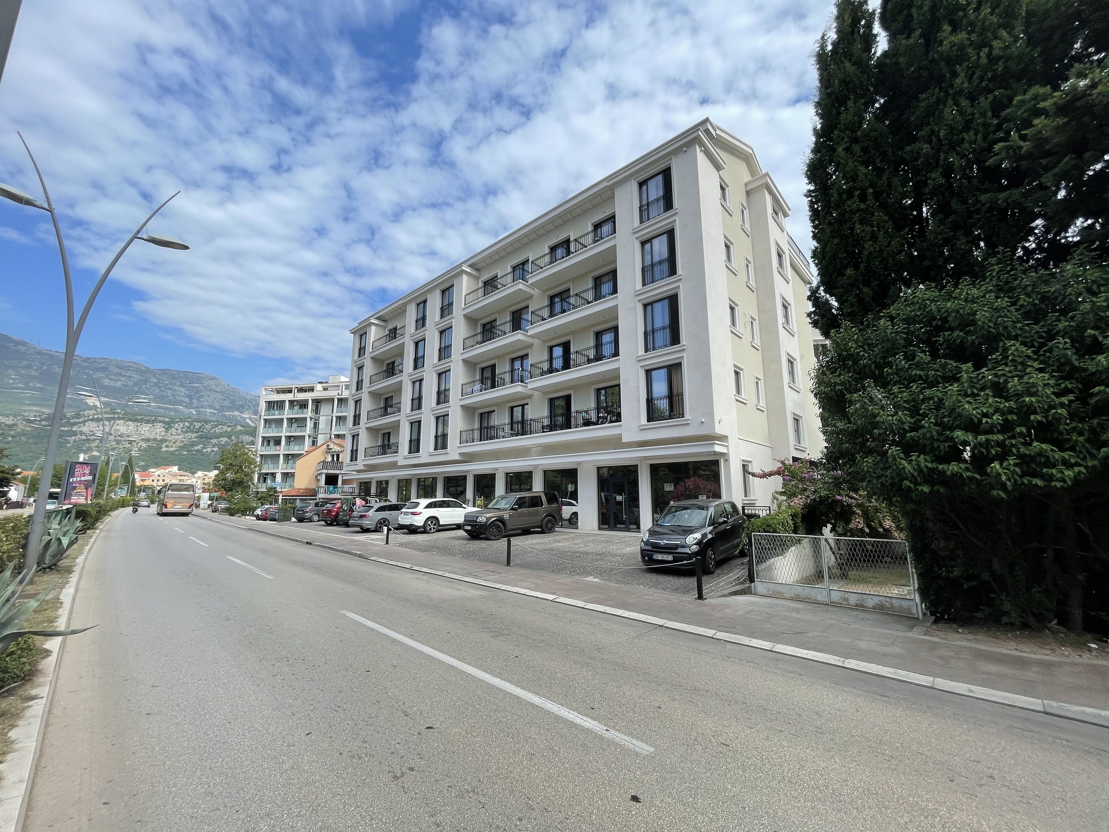A multi-story hotel with balconies, a parking area, and a road with vehicles.