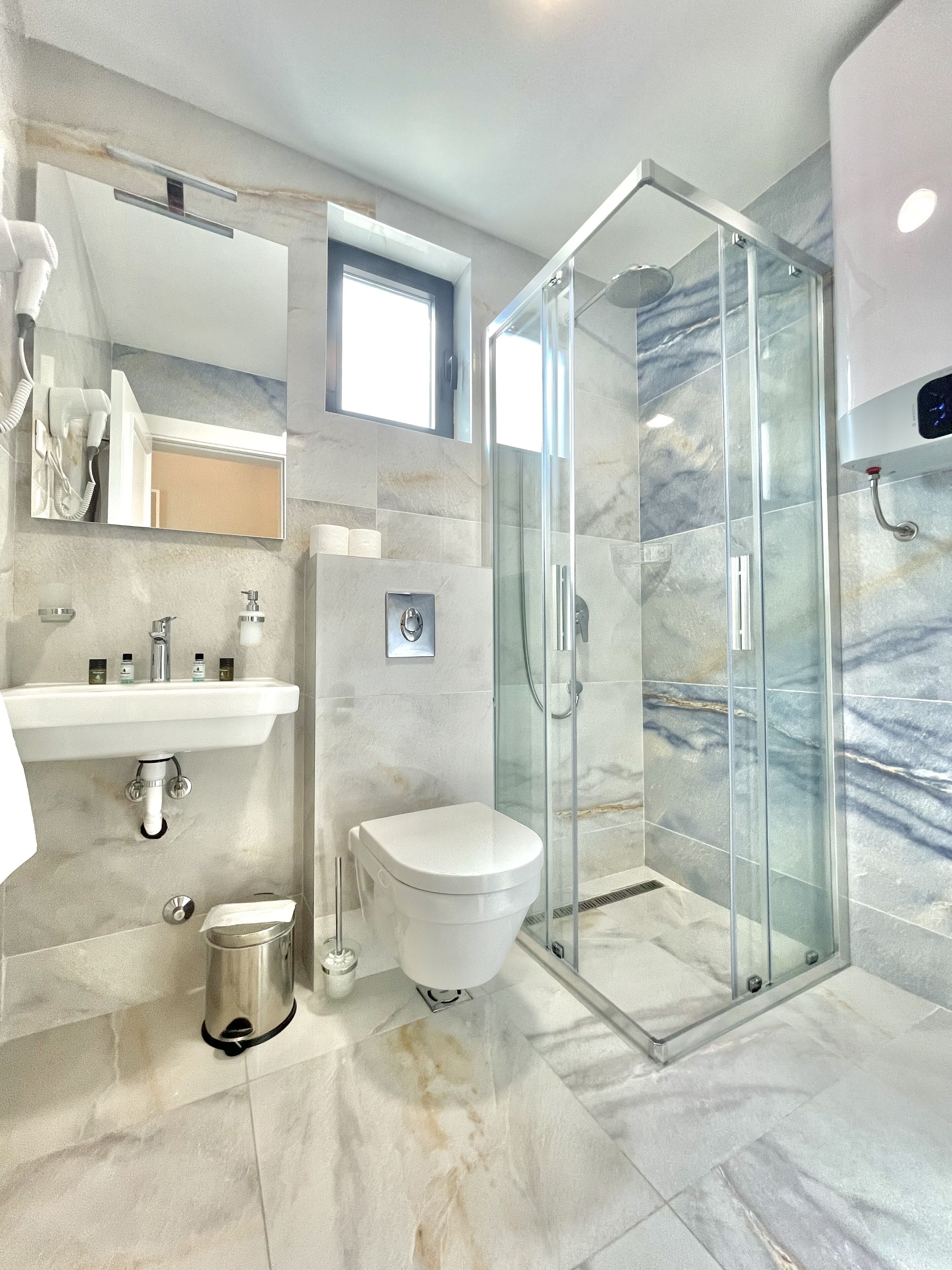 A modern bathroom with a glass shower enclosure, a white toilet, and a marble-tiled floor.