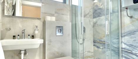 A modern bathroom with a glass shower enclosure, a white toilet, and a marble-tiled floor.