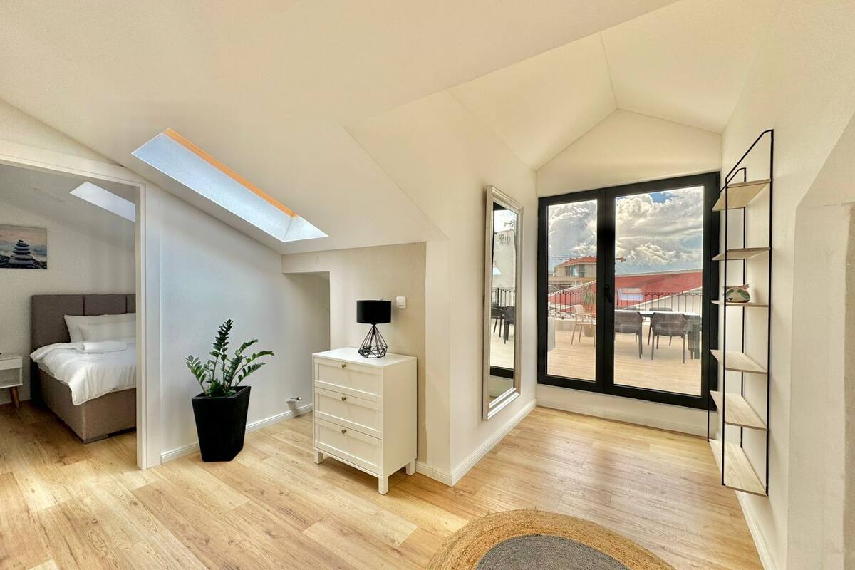 A spacious room with a bed, a potted plant, a desk, and a large window offering a view of the outside.