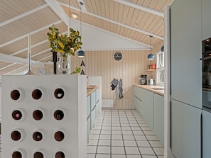 Een moderne keuken met betegelde vloer, houten balken in het plafond en hangende lampen.