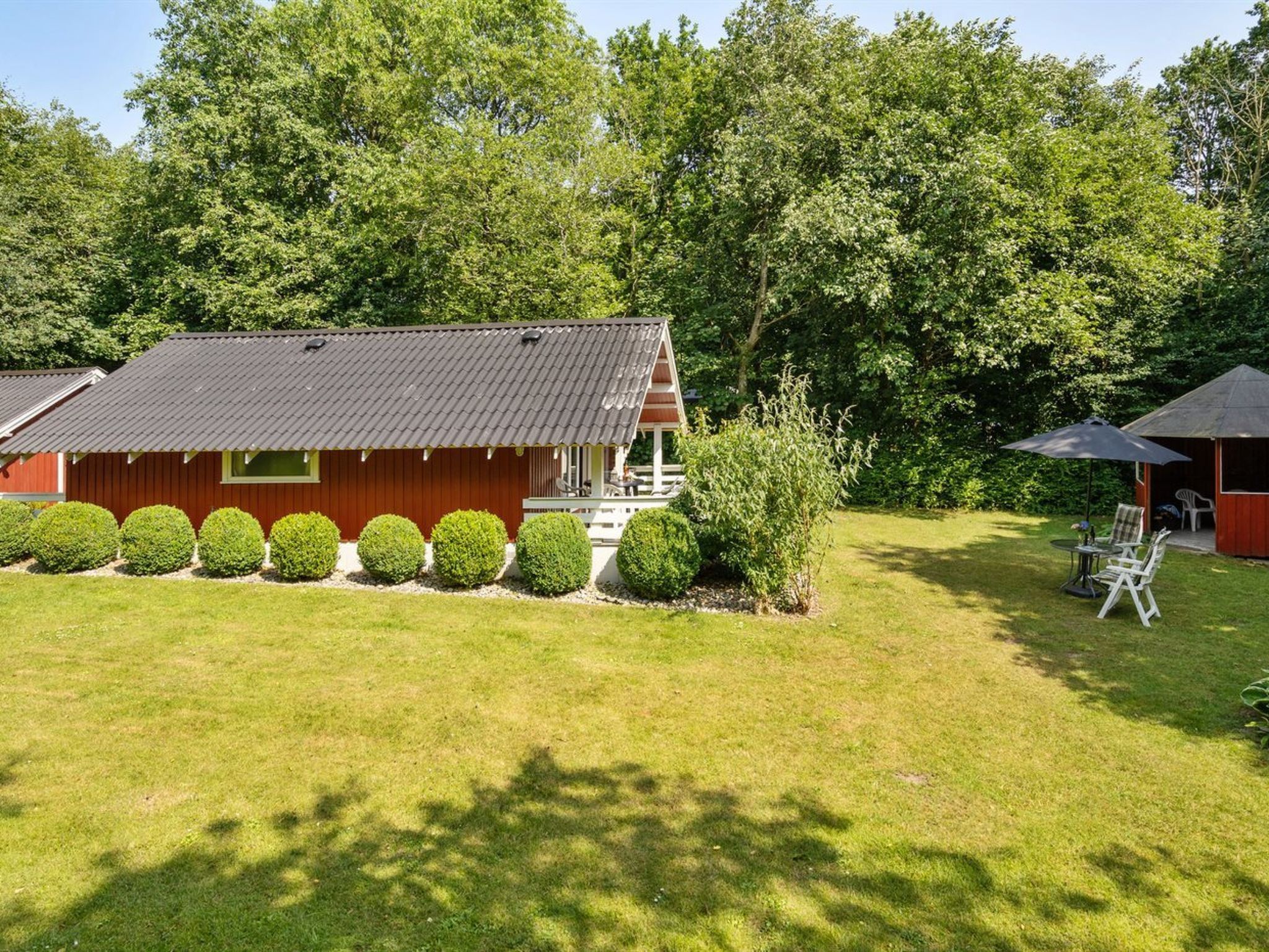 Een rood gebouw met een schuin dak, omgeven door een verzorgd gazon en keurig bijgesnoeide struiken.