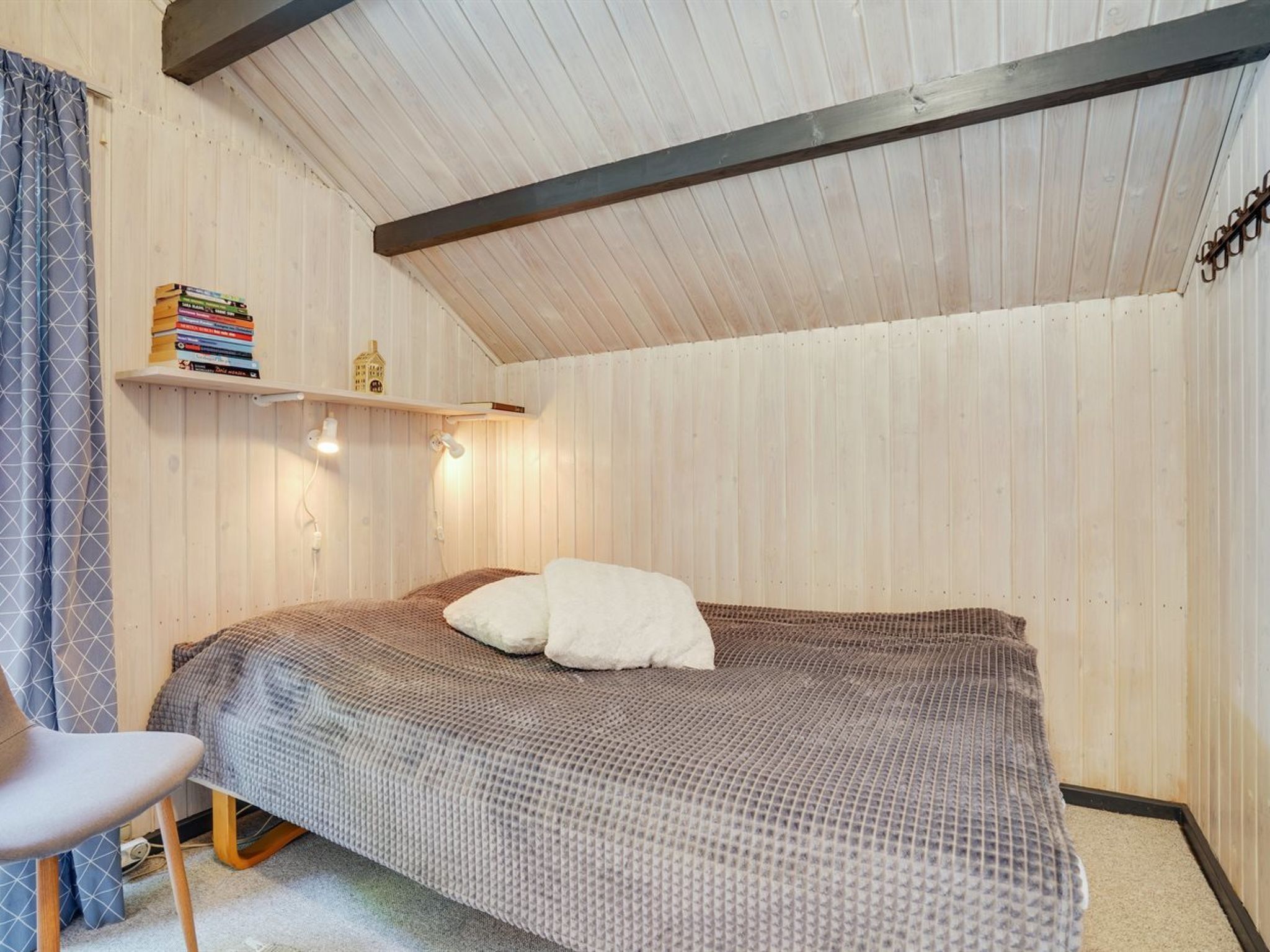 A bedroom with a bed, a chair, a shelf with books, and a small decorative item.