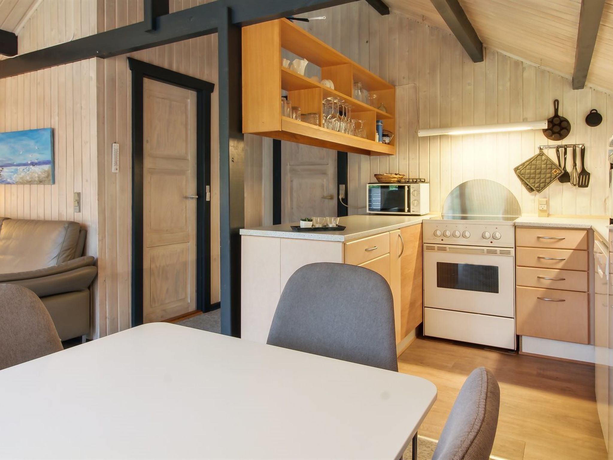 A compact kitchen with a microwave, oven, and wooden shelves above the counter.