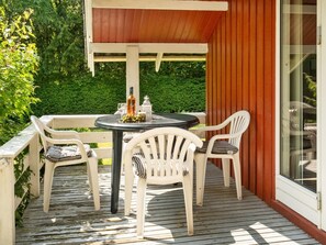 A wooden deck with a round table and two chairs, a bottle, and a glass.