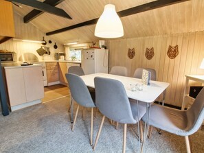 A compact kitchen with modern appliances, a dining area with a white table and grey chairs, and wooden accents on the walls.