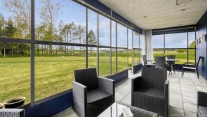 A covered outdoor seating area with wicker furniture and large windows overlooking a grassy field. - "Mikkeline" - 400m to the fjord by Interhome (Øster Assels)