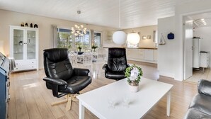 A modern living room with two black leather chairs, a white coffee table, and a dining area with white chairs and a chandelier. - "Mikkeline" - 400m to the fjord by Interhome (Øster Assels)