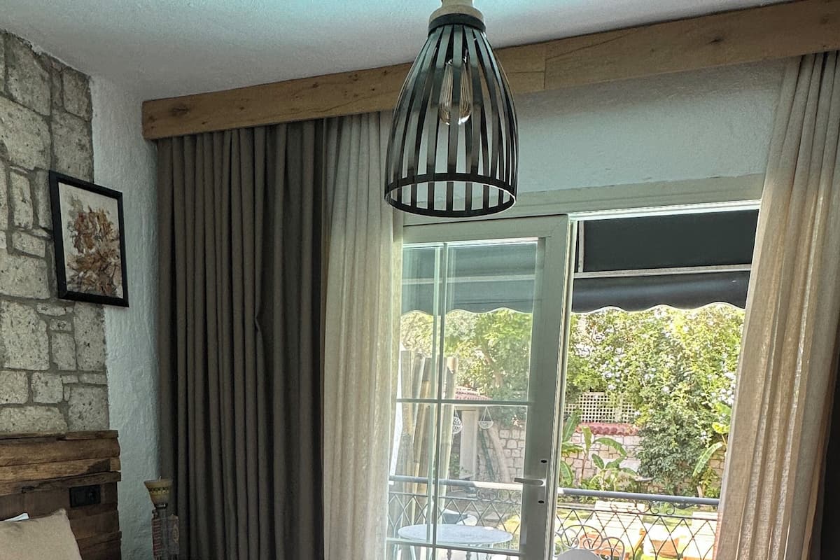 A bedroom with a large bed, a wooden headboard, a hanging light fixture, and a view of a swimming pool through a glass door.
