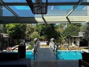 A pool area with a wooden deck leading to the water, surrounded by greenery and outdoor furniture. - Argente Alacatı Adult Only (Cesme)