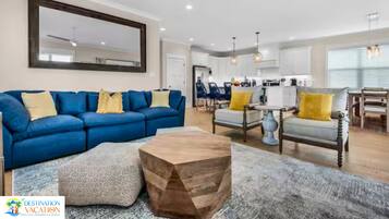 Un salon moderne avec un canapé bleu, une table basse en bois et un coin repas agrémenté d’un lustre.