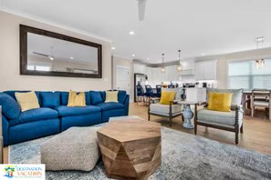 Un salon moderne avec un canapé bleu, une table basse en bois et un coin repas agrémenté d’un lustre.