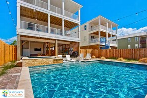 A two-story building with a swimming pool, outdoor seating, and a wooden fence.