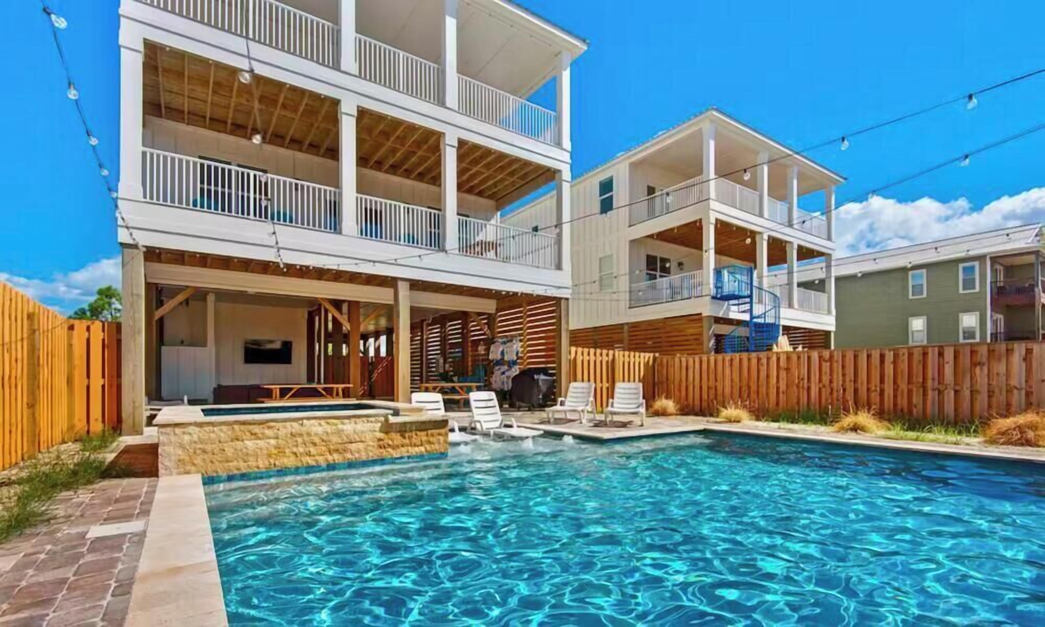 A two-story building with a swimming pool, outdoor seating, and a wooden fence.