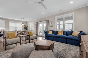 A spacious living room with a blue sofa, two armchairs, a coffee table, and a dining area with a table and chairs.