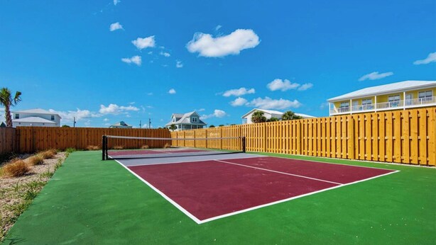 Ein Tennisplatz im Freien mit Holzumzäunung und Häusern im Hintergrund.