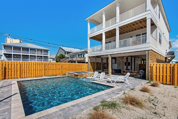 A two-story house with a pool, outdoor seating, and a wooden fence.