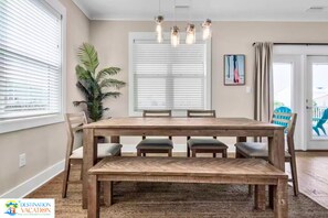 A dining area with a wooden table and benches, a potted plant, and a window with blinds.