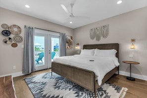 A bedroom with a large bed, a ceiling fan, a view through a glass door, and a patterned rug.