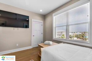 A bedroom with a bed, a television mounted on the wall, a window with blinds, and a door.
