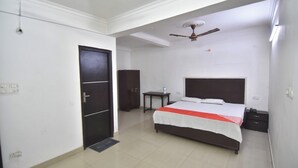 A bedroom with a bed, a nightstand, a wardrobe, a ceiling fan, and a door. - Royal Guest House (Noida)