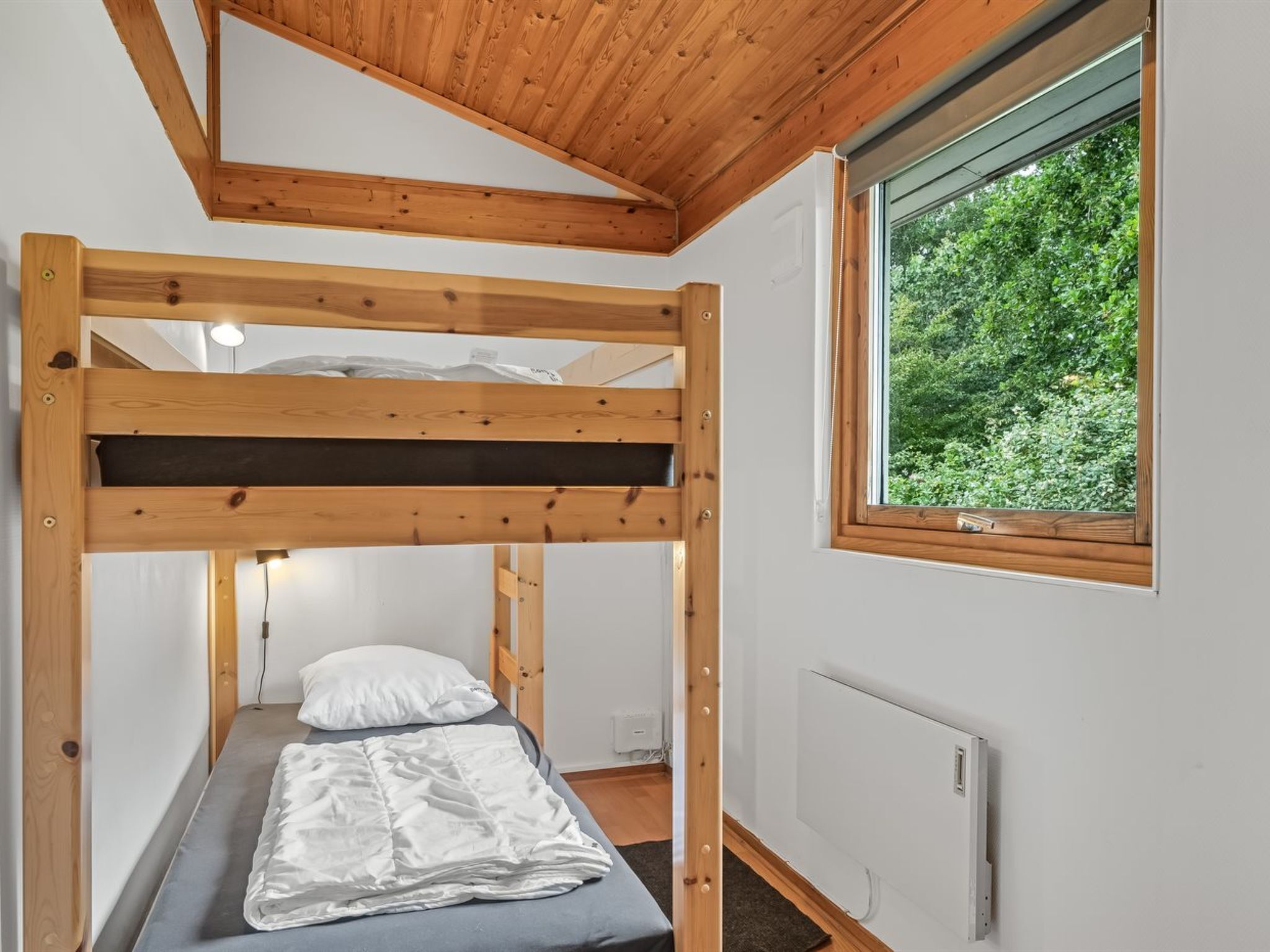 Une chambre avec un lit superposé et une fenêtre donnant sur un espace verdoyant.