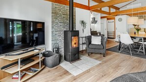 Ein modernes Wohnzimmer mit großem Fernseher, Kamin, Holzbalken und einer Wand aus Stein.