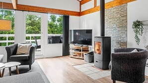 Ein modernes Wohnzimmer mit Steinwand, Holzbalken, Fernseher, Kamin und einem Balkon mit Gartenmöbeln.