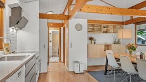 Eine moderne Küche mit Holzbalken, einem Essbereich mit weißen Stühlen und Blick ins Freie.