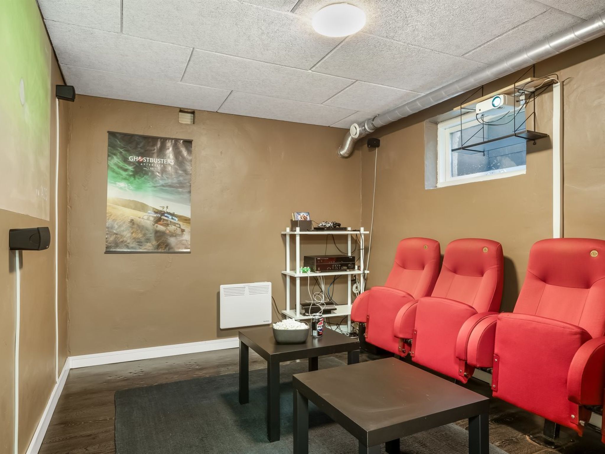 A room with a projector screen, a poster, a white shelf with electronic devices, and three red chairs.
