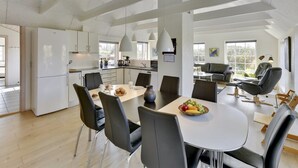 Een moderne keuken met witte kasten, een eetgedeelte met een ronde tafel, en een zithoek met een bank en stoelen.