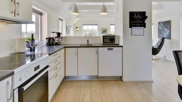 Een moderne keuken met een ingebouwde oven, magnetron en vaatwasser. Er zijn hanglampen, een spoelbak en een raam dat natuurlijk licht biedt.